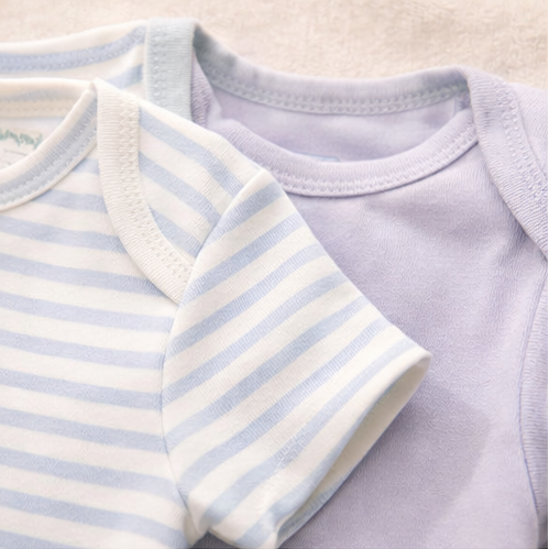 Collection of baby clothing items including a onesie with a bear face and 'bear sweet' text, striped shirt, and patterned fabric with animal designs.