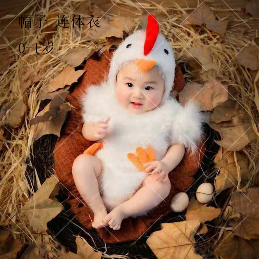 Baby in white chicken jumpsuit costume with matching hat sitting in nest
