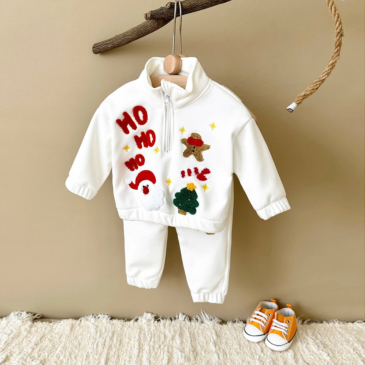Cream zip-neck top and matching pants with Santa, gingerbread, tree appliques, and HO HO HO lettering, displayed on a hanger.