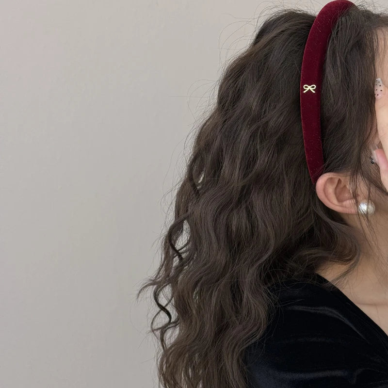 Burgundy padded headband with a small gold-colored bow accent, shown worn in curly hair.