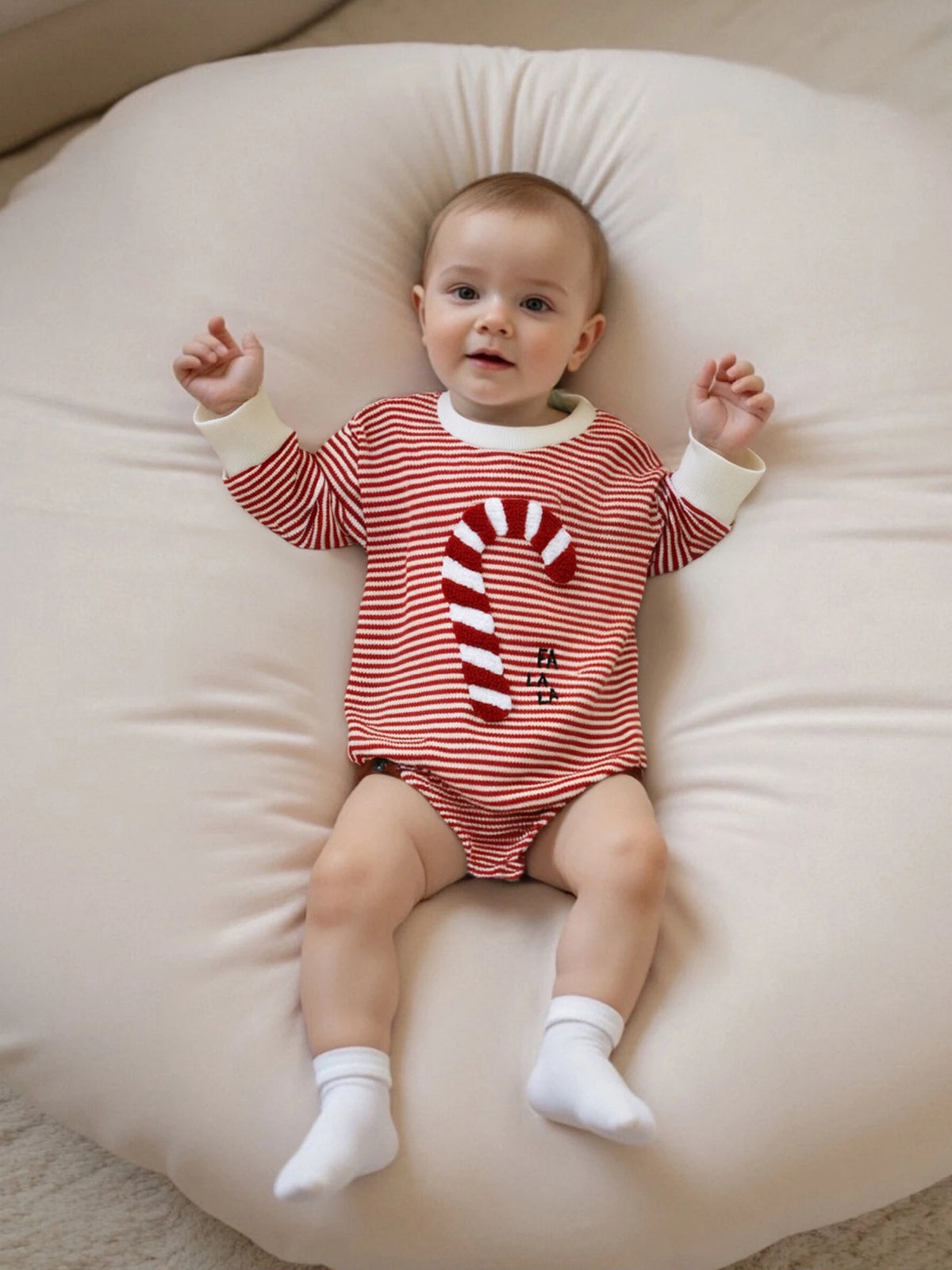 Baby wearing a red-and-white striped long-sleeve bubble romper with a large candy cane applique and white cuffs.