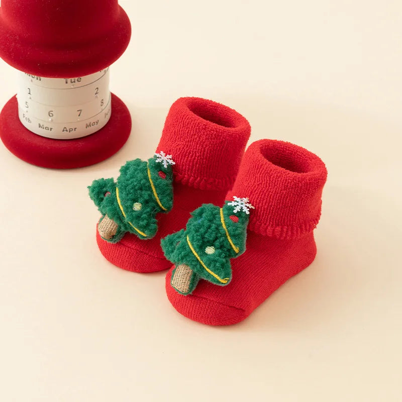 Red baby socks with folded cuffs and raised green Christmas tree decorations.