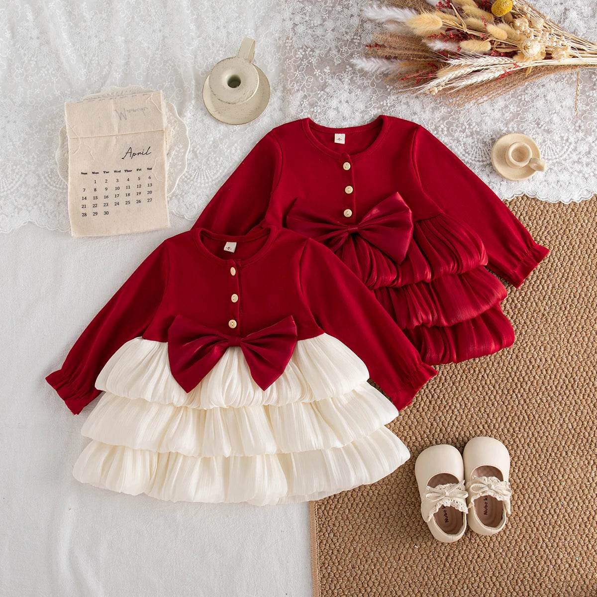 Two long-sleeve dresses with red bodices, front buttons, large waist bows, and tiered skirts in cream and red.