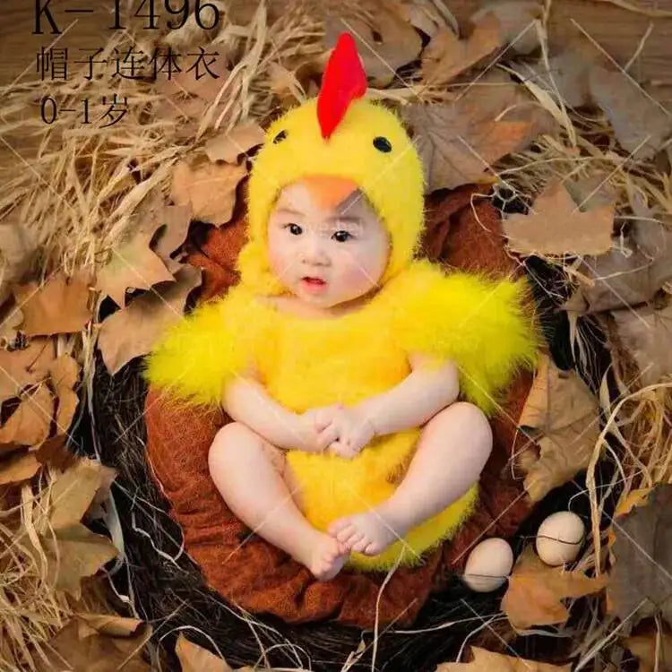 Baby in yellow chicken jumpsuit costume with matching hat sitting in nest