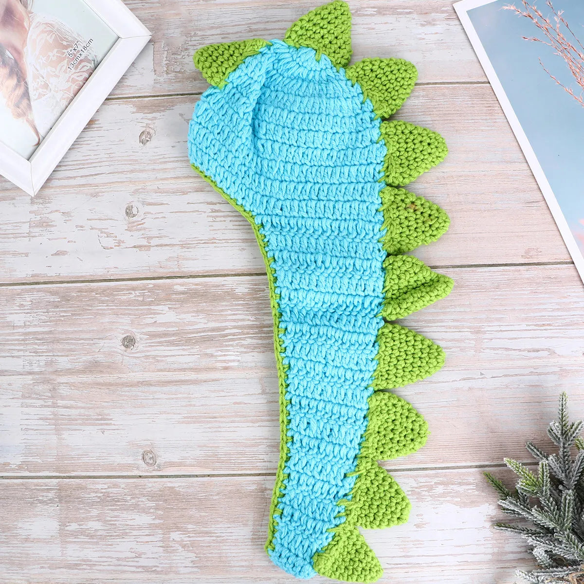 Blue crochet dinosaur tail with green spikes on wooden surface