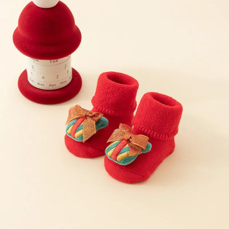 Red baby socks with folded cuffs and multicolored present decorations topped with gold-colored bows.