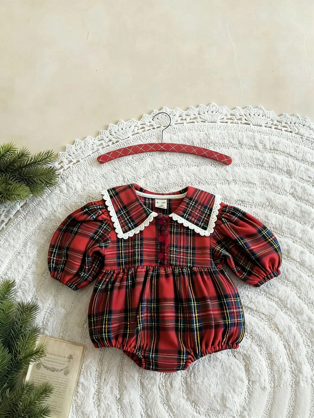 Red plaid baby bodysuit with a white lace-trimmed collar, long puff sleeves, and gathered leg openings.