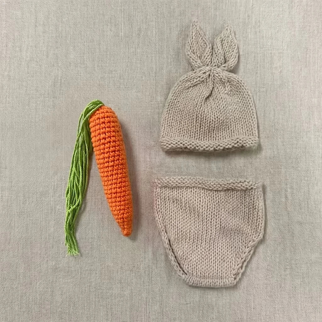 Beige knit baby rabbit hat with ears, knit diaper cover, and orange knit carrot prop laid flat on beige background