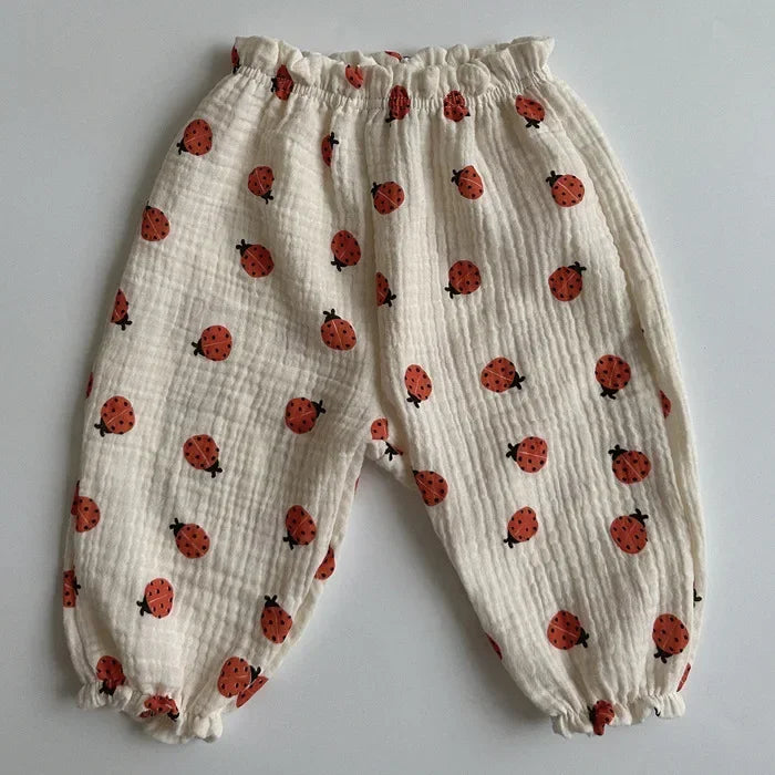 White children's pants with red ladybug pattern on a gray background