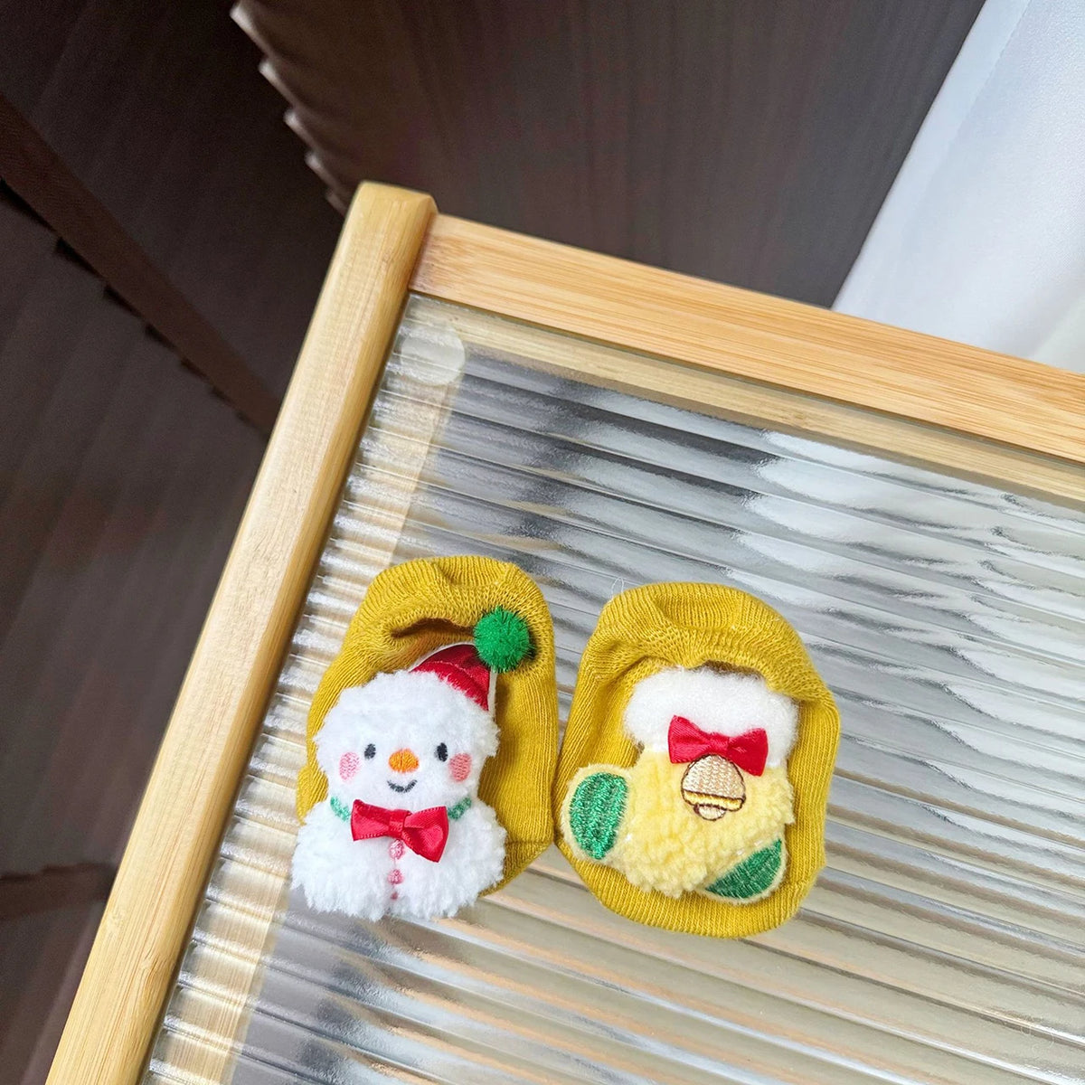 Yellow baby socks with a textured snowman on one sock and a stocking with a red bow and bell detail on the other.