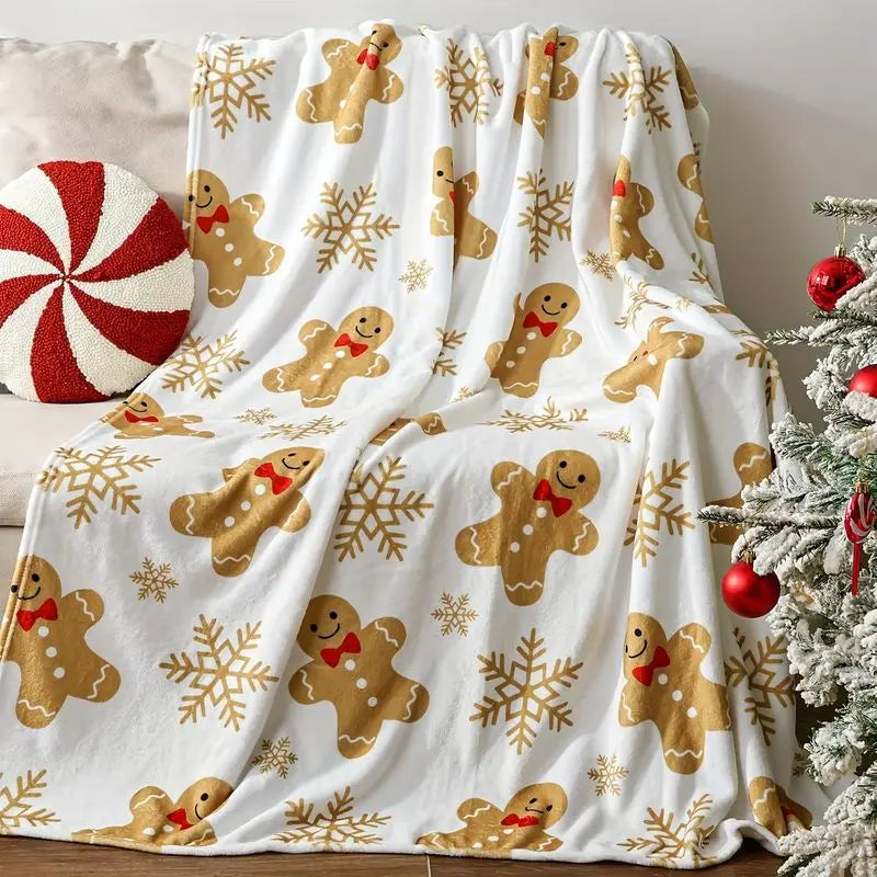 White throw blanket with gingerbread figures, red bow ties, and gold-colored snowflakes, draped over a sofa.