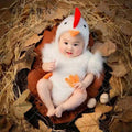 Baby in white chicken jumpsuit costume with matching hat sitting in nest