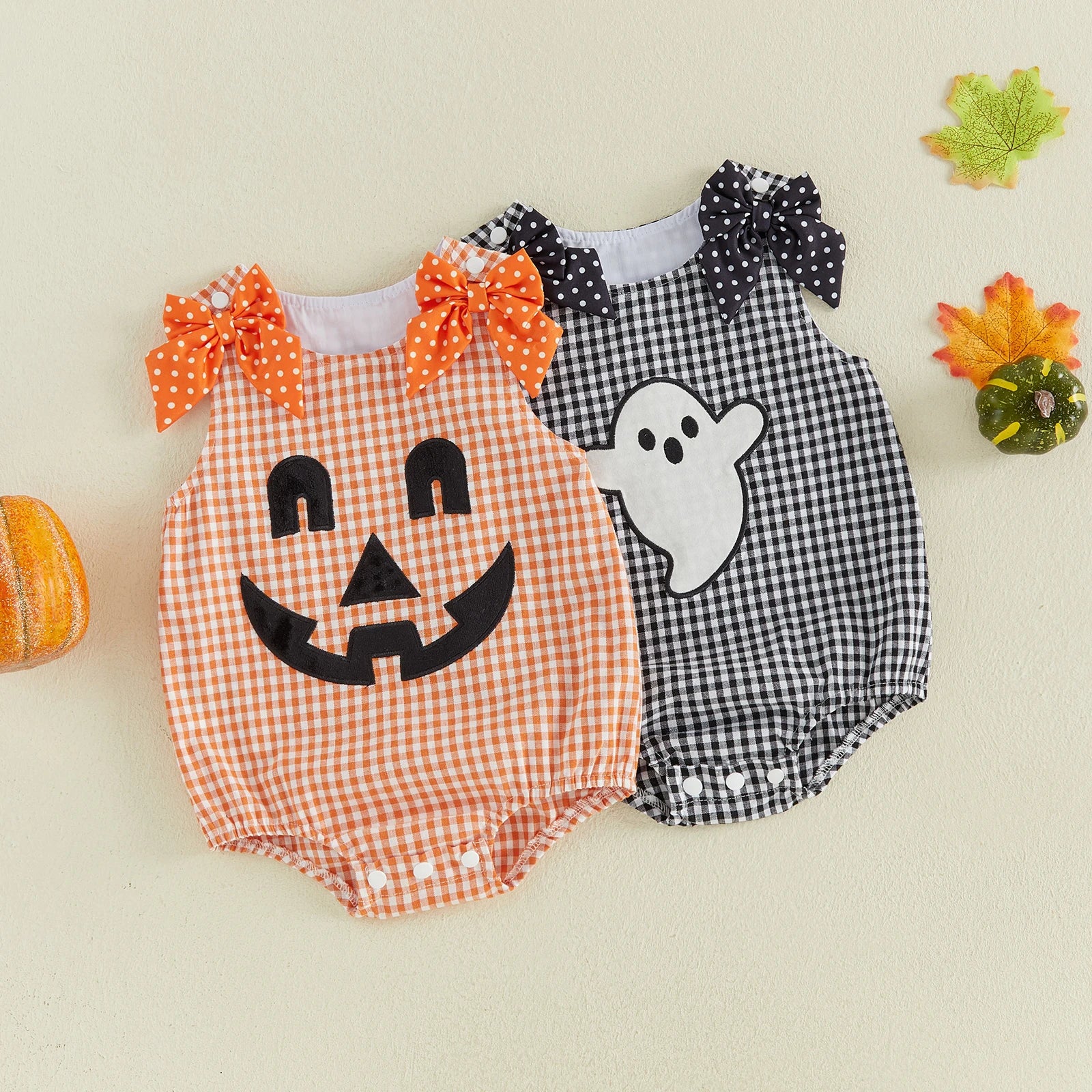 Two baby rompers side by side, one orange plaid with jack-o'-lantern face and one black and white plaid with ghost applique