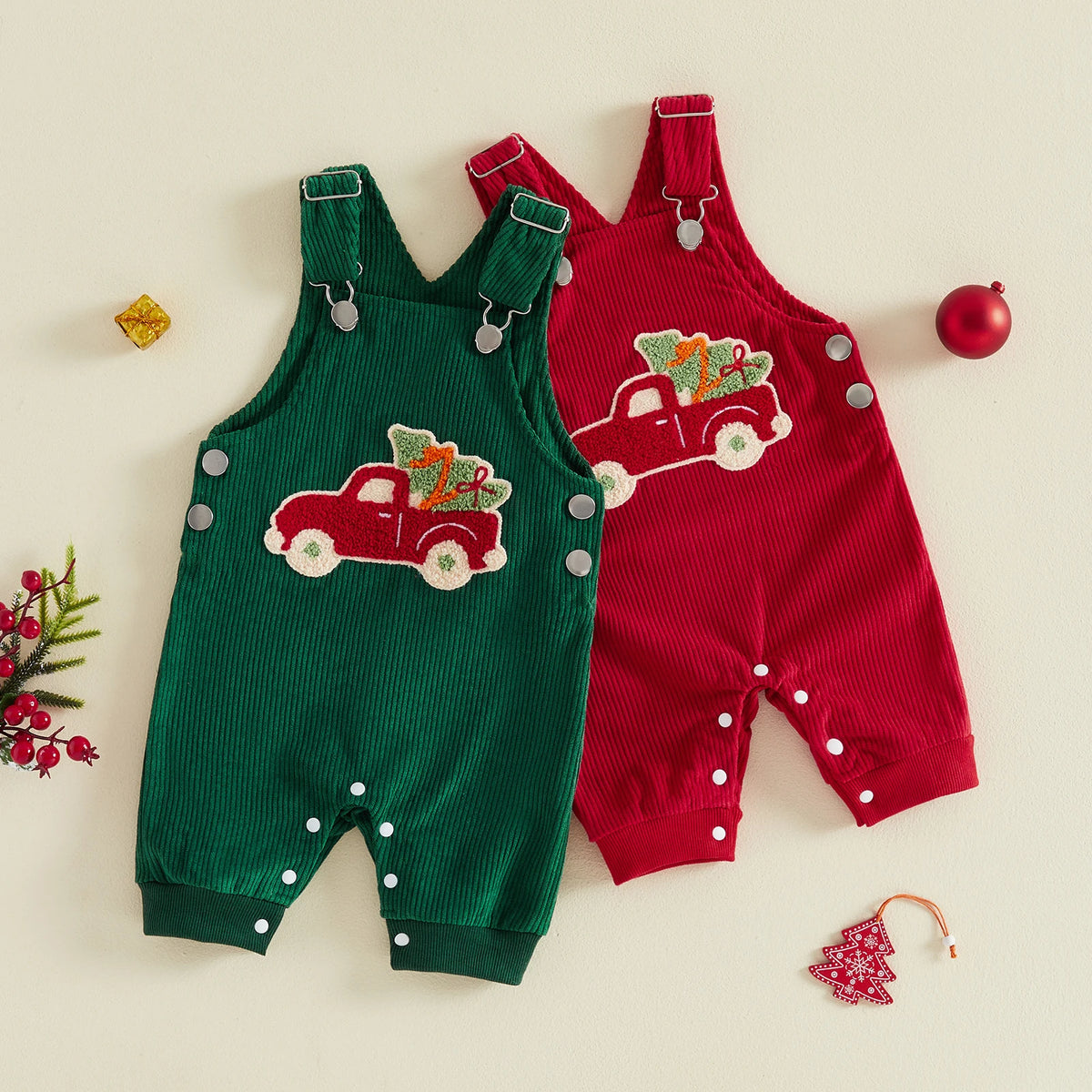 Green and red baby overalls with red truck and Christmas tree appliques, adjustable shoulder straps, and snaps along the legs.