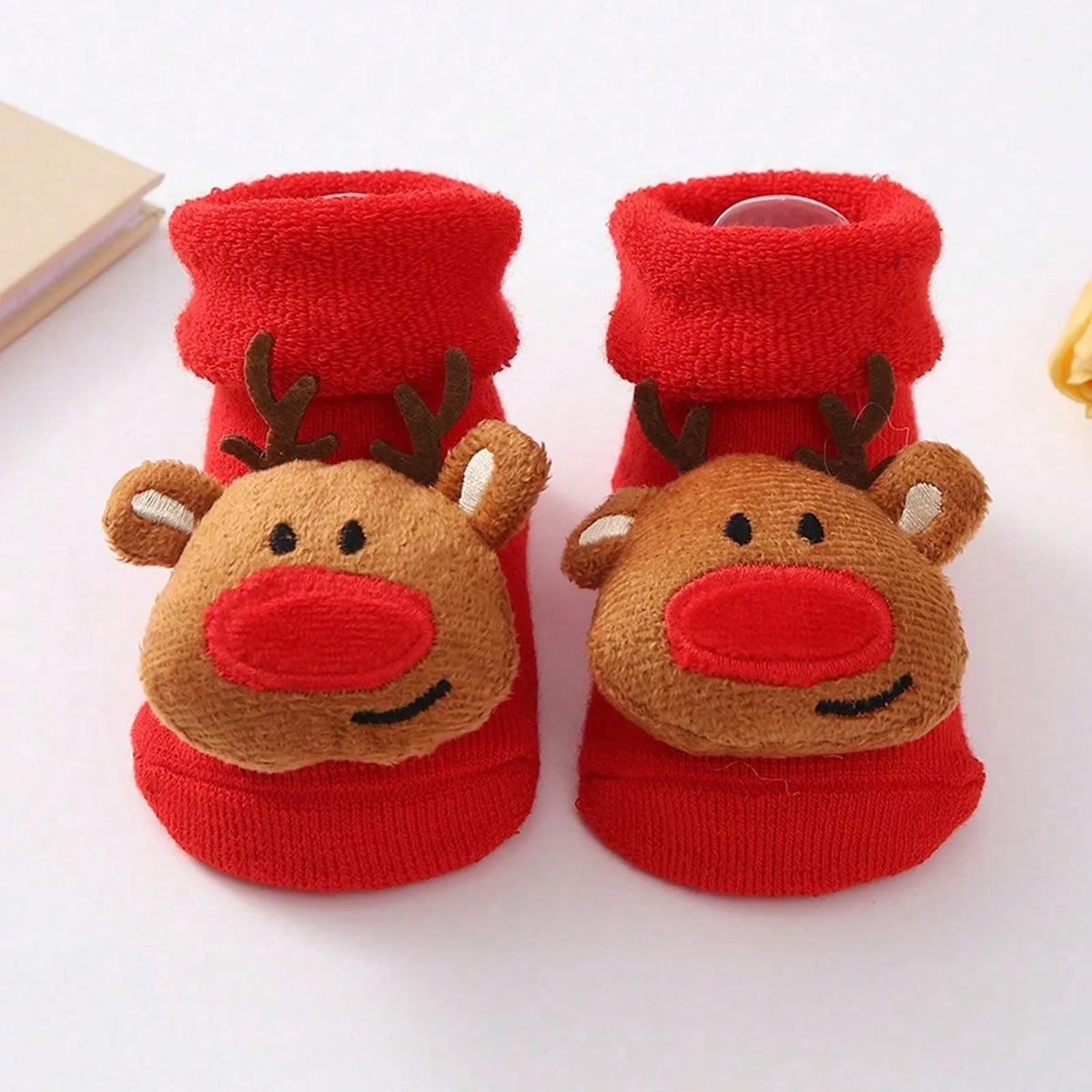 Red cuffed baby socks with brown smiling reindeer faces, large red noses, and dark antlers.