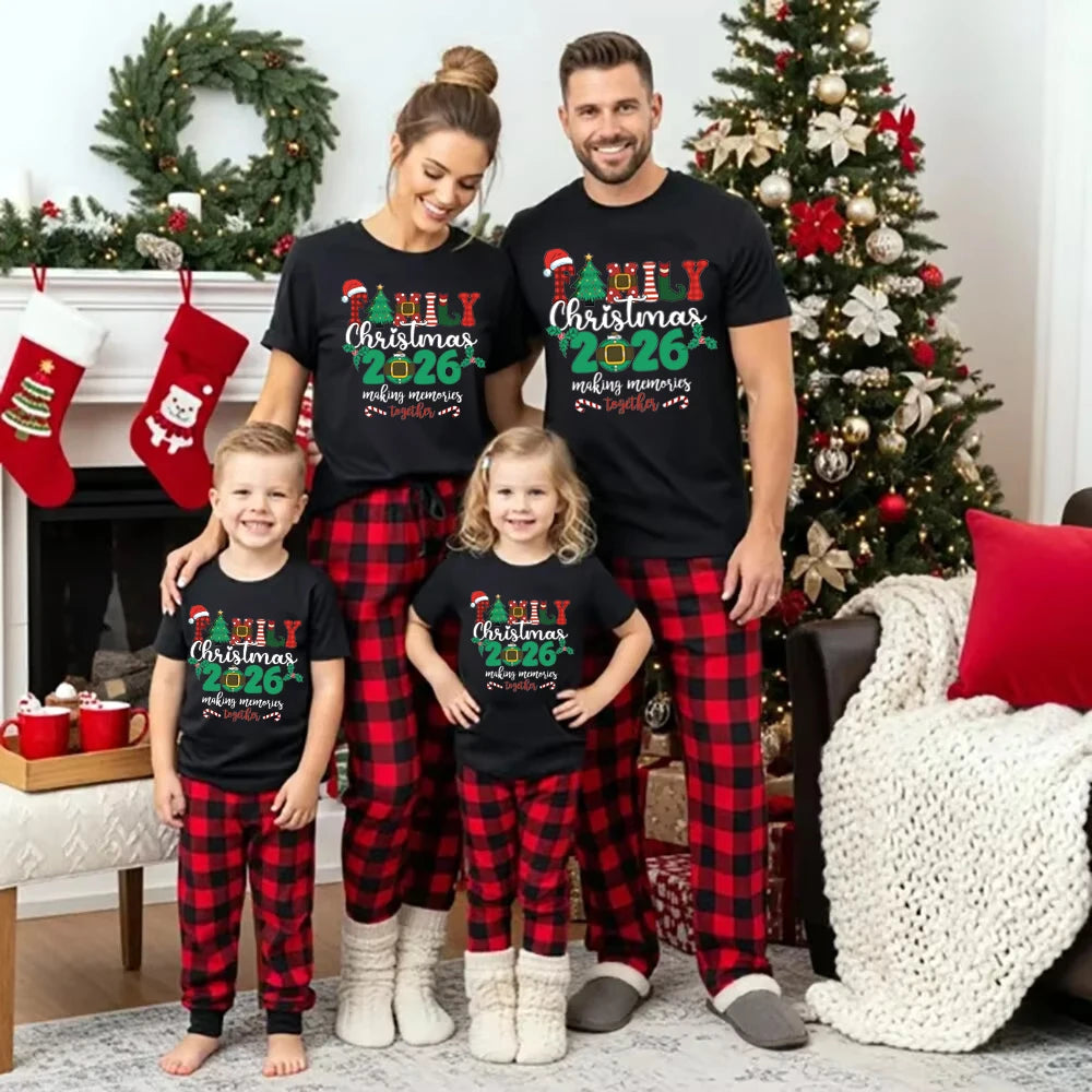 Two adults and two children wearing black Christmas 2026 graphic T-shirts, styled with red-and-black plaid pants.