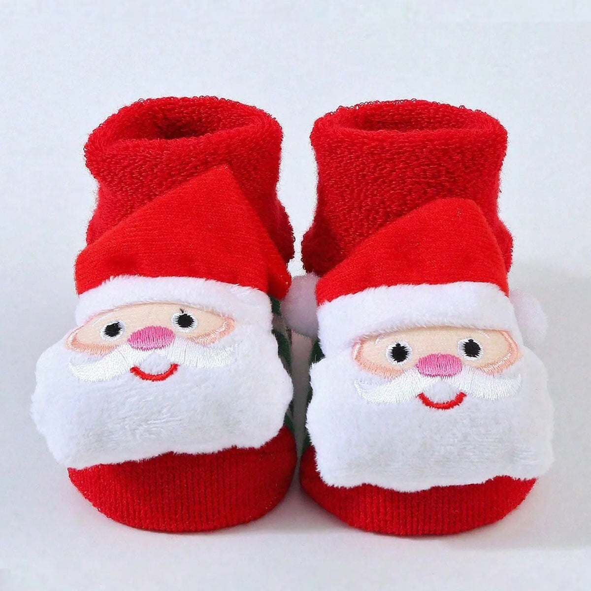 Red cuffed baby socks with smiling Santa faces, white beards, pink noses, and red hats.