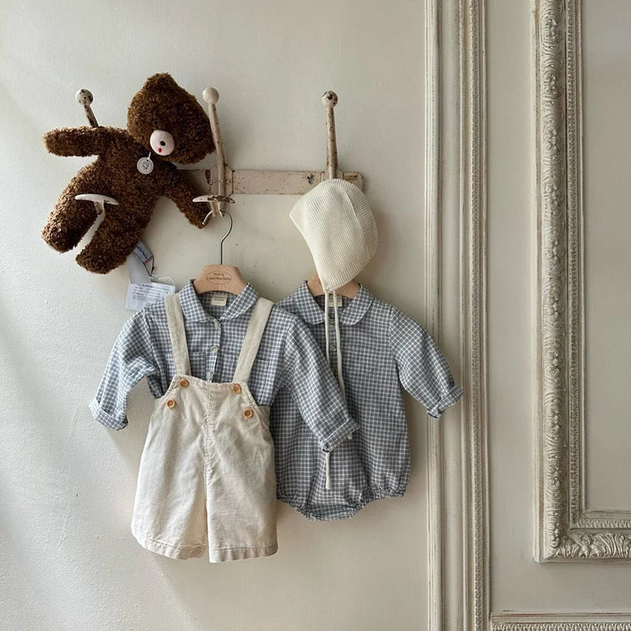 Blue check baby romper styled with ivory overalls and a knit bonnet