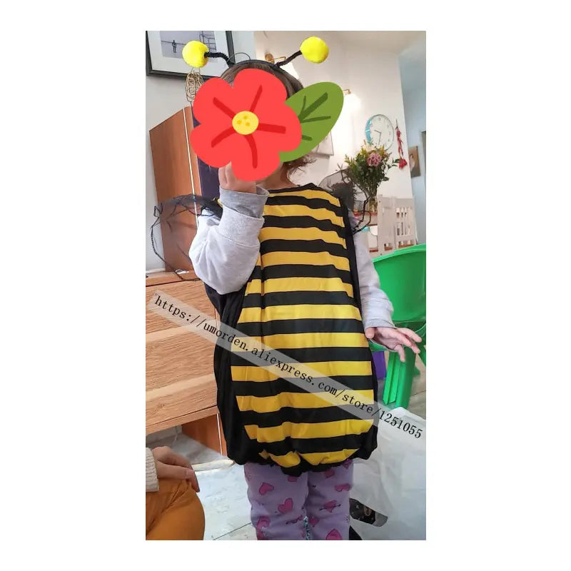 Child wearing bumblebee costume indoors with face covered by flower sticker