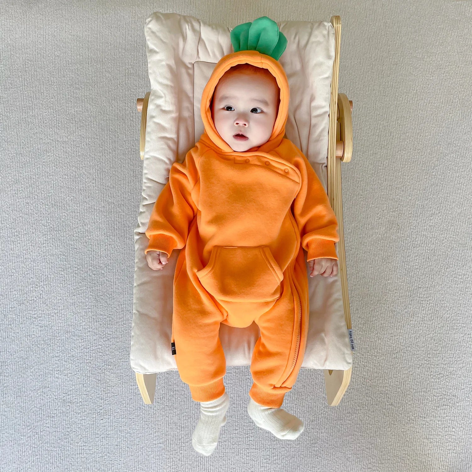 Baby in carrot costume jumpsuit lying on baby chair back view