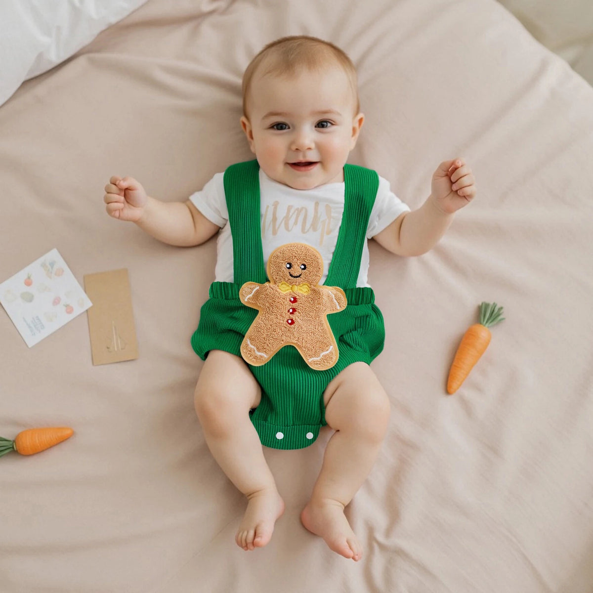 Baby wearing green ribbed suspender-style overalls with a large gingerbread applique, layered over a white T-shirt.