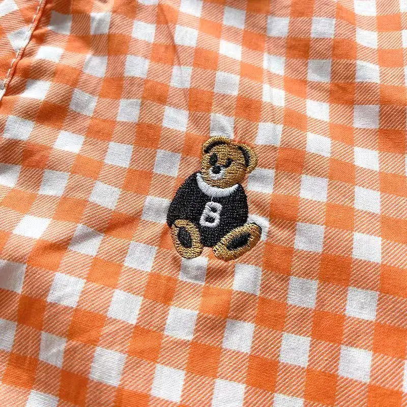 Embroidered teddy bear patch detail on orange plaid shirt