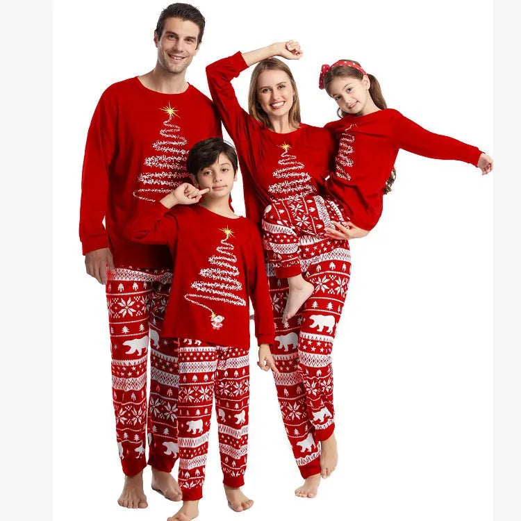 Two adults and two children wearing red pajama tops with spiral Christmas trees and red-and-white patterned pants.
