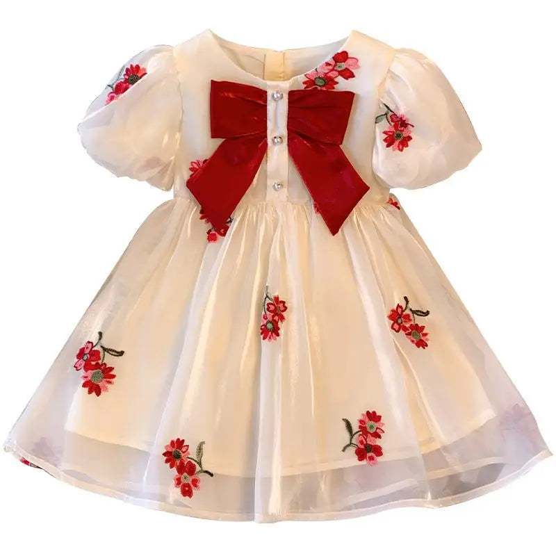 Cream dress with red floral embroidery, a large red bow, short puff sleeves, and a sheer skirt overlay.
