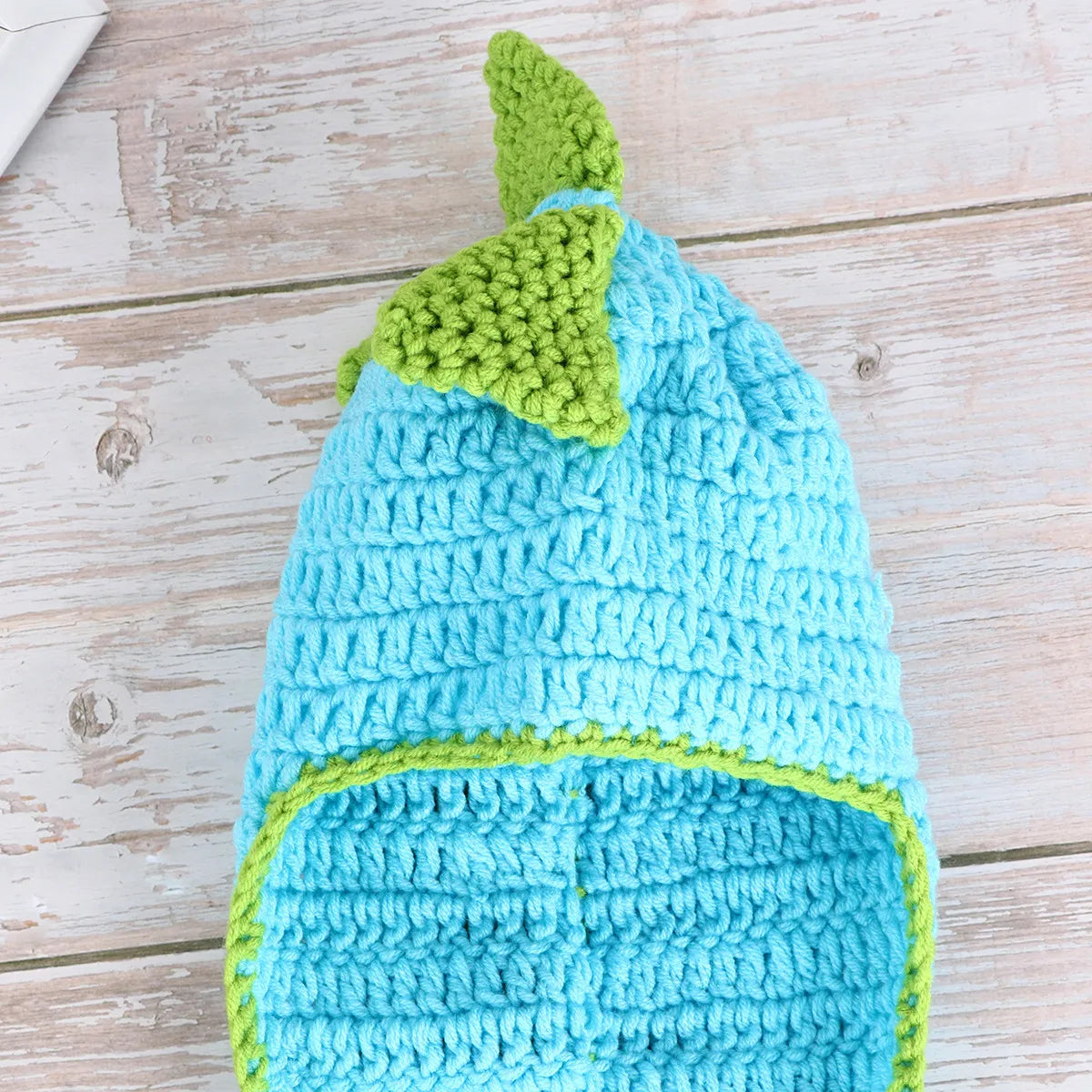 Blue crochet dinosaur hat with green spikes on wooden surface