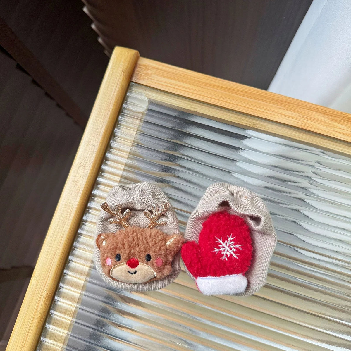 Pair of beige baby socks with a reindeer face on one sock and a red mitten with a white snowflake on the other.
