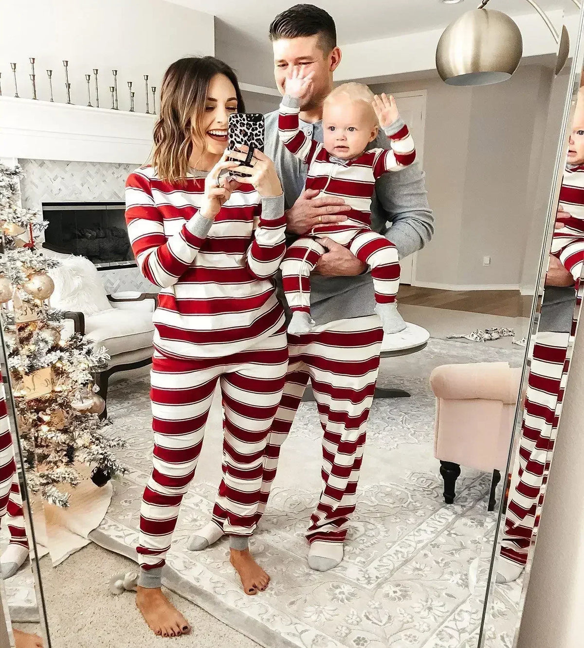 Two adults and a baby wearing coordinated cranberry-and-cream striped pajamas with gray trim.