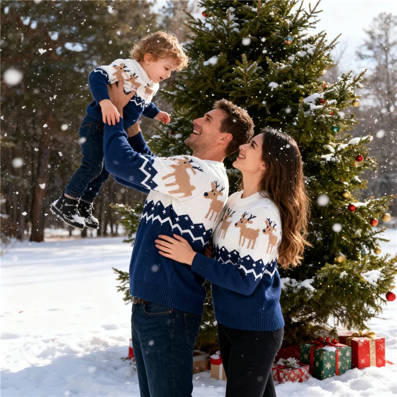 Two adults and a child wearing navy sweaters with white reindeer-patterned yokes beside a Christmas tree.