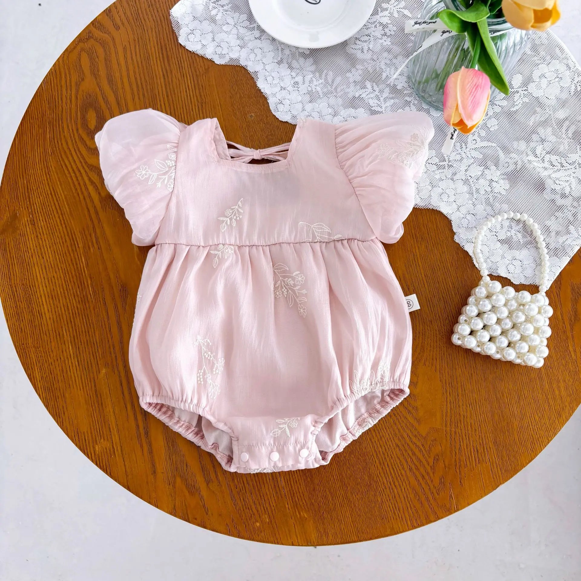 Pink baby romper displayed on a hanger showing short sleeves and square collar
