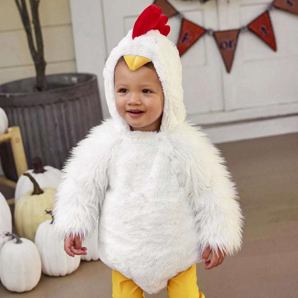 Toddler wearing white chick costume outdoors with pumpkins