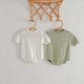 Beige and soft green openwork knit baby rompers on wooden hangers