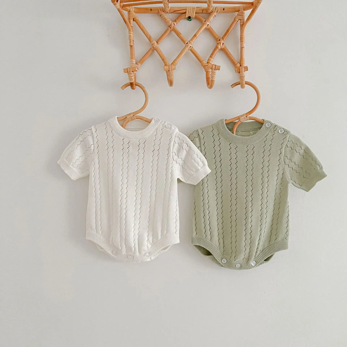 Beige and soft green openwork knit baby rompers on wooden hangers