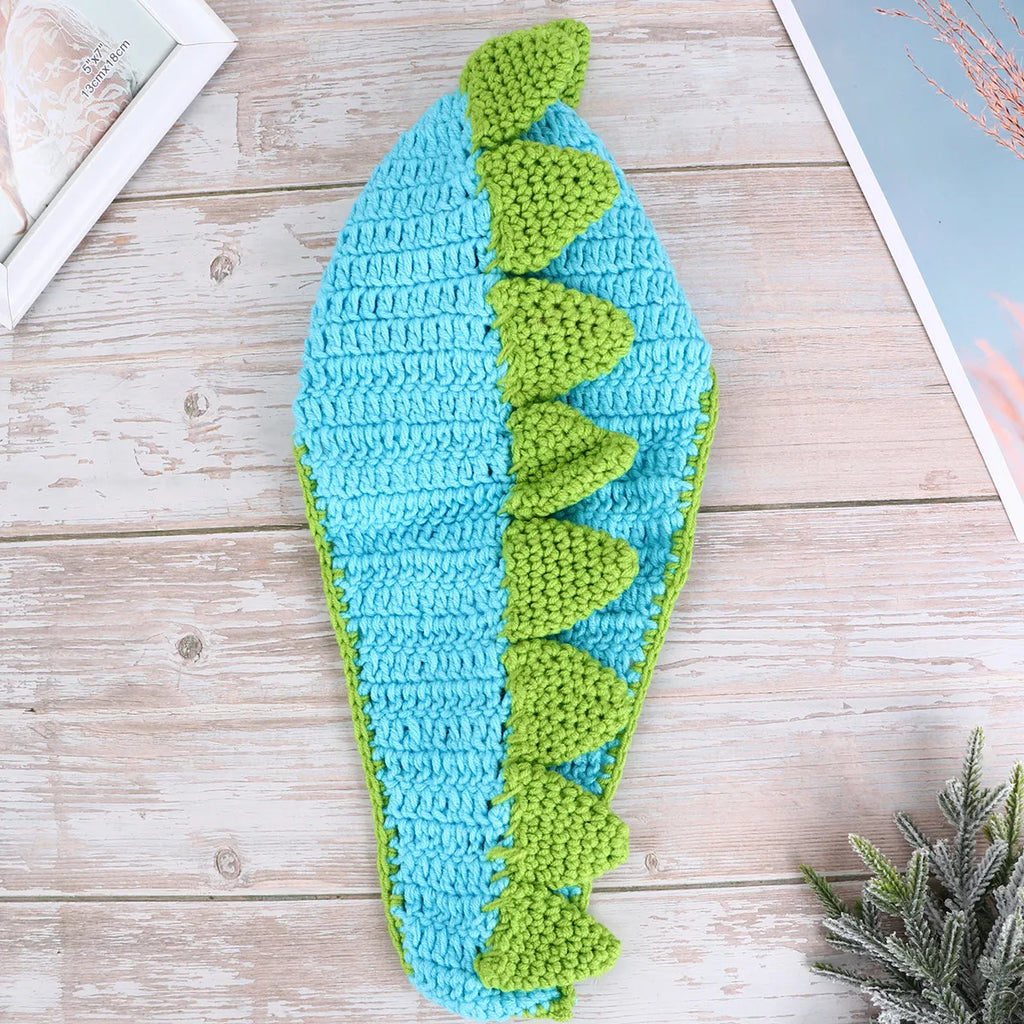 Blue crochet dinosaur hat with green spikes on wooden surface