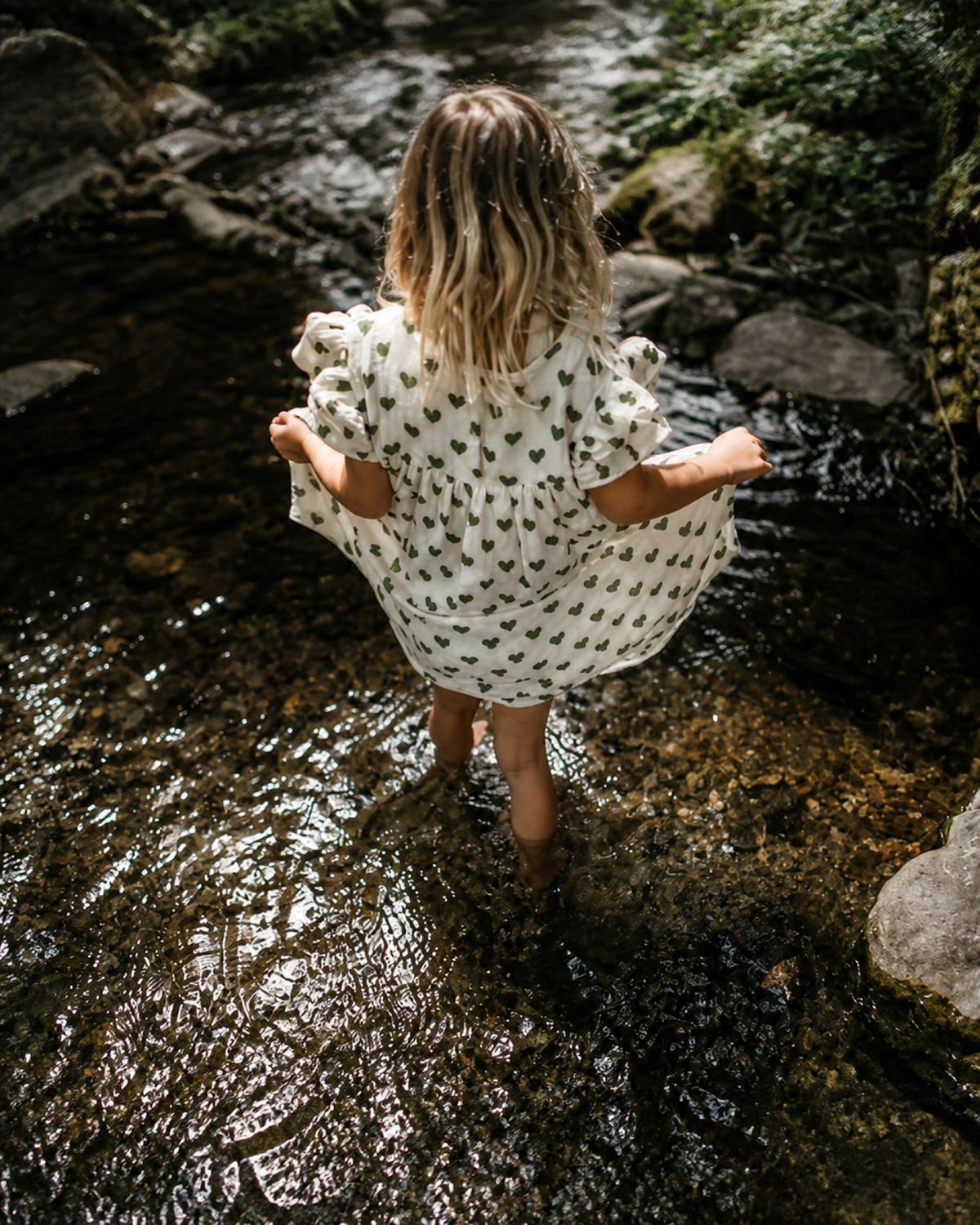 Girl wearing the Élodie Heart Summer Dress in a woodland stream