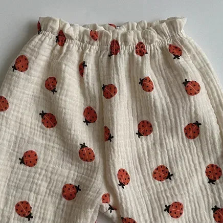 White children's pants with red ladybug pattern on a gray background